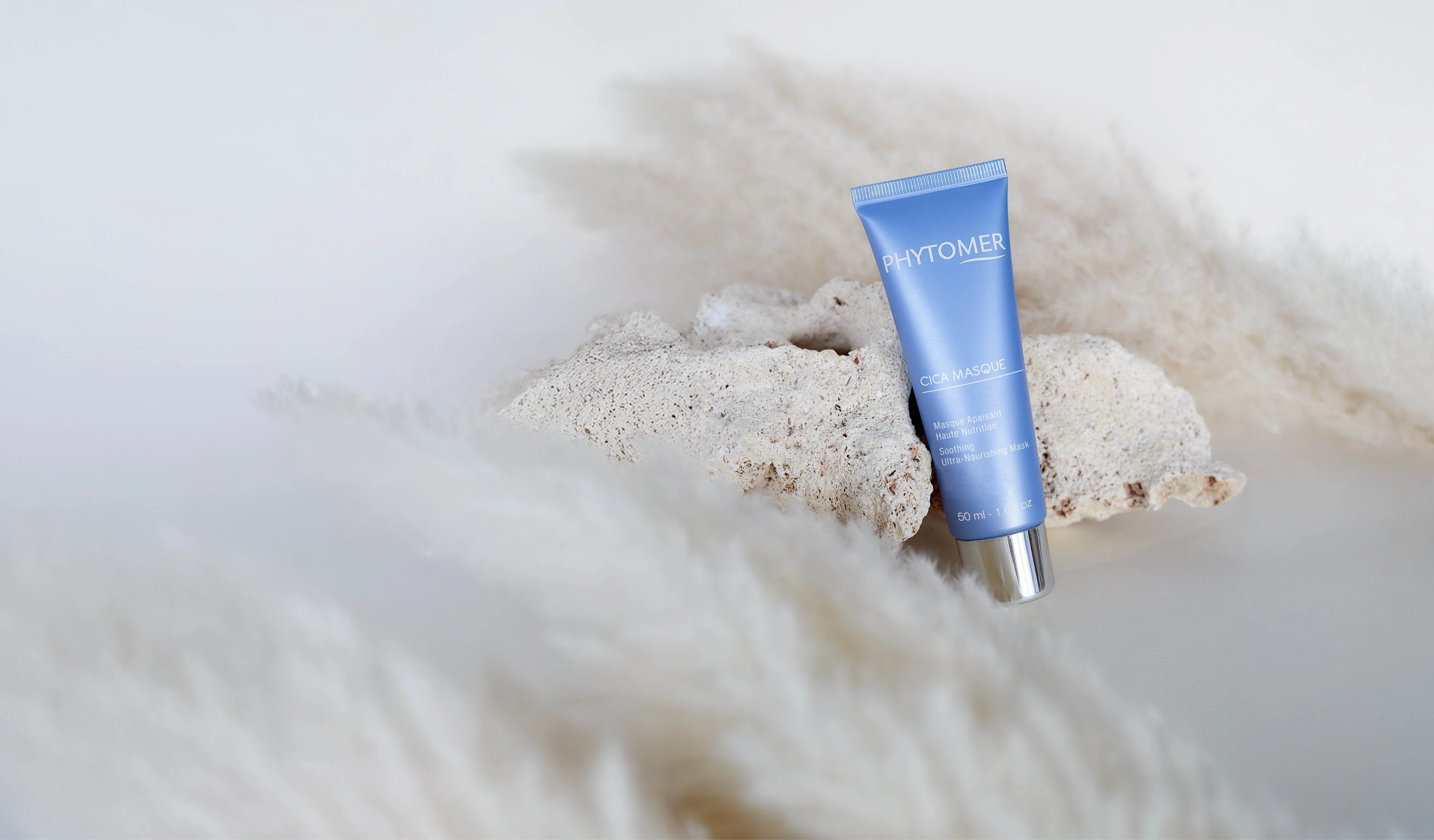 Cica Masque Soothing Ultra-Nourishing Mask, 50 ml tub on a rock with feathers around it.