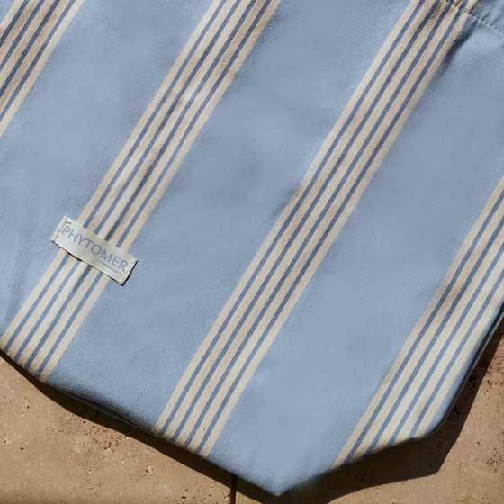 Blue Phytomer tote bag with white stripes laying on a tan countertop.