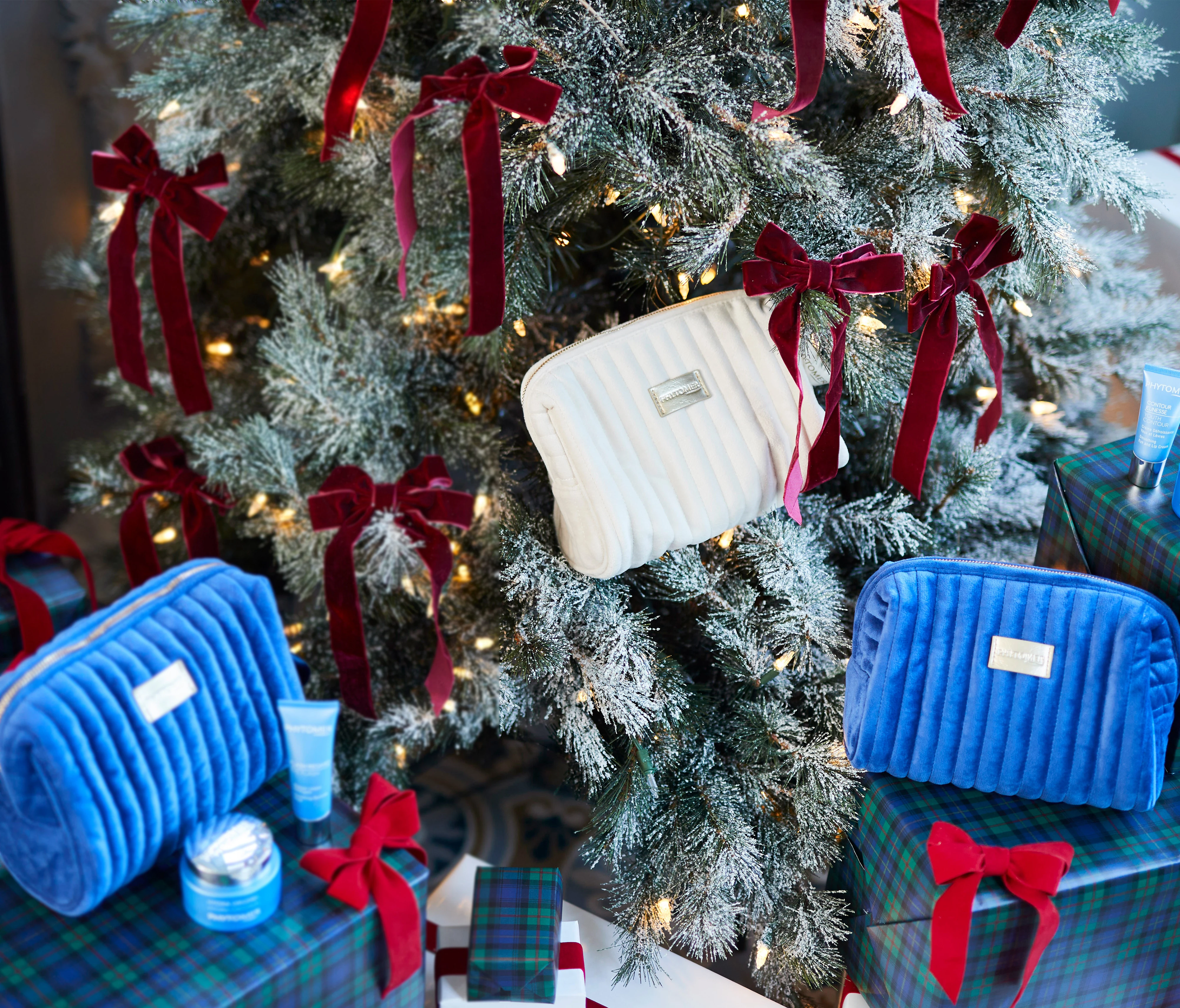 An assortment of Phytomer's Holiday Gifts sets in a velvet beauty pouch, sitting on top of gift boxes around a tree.