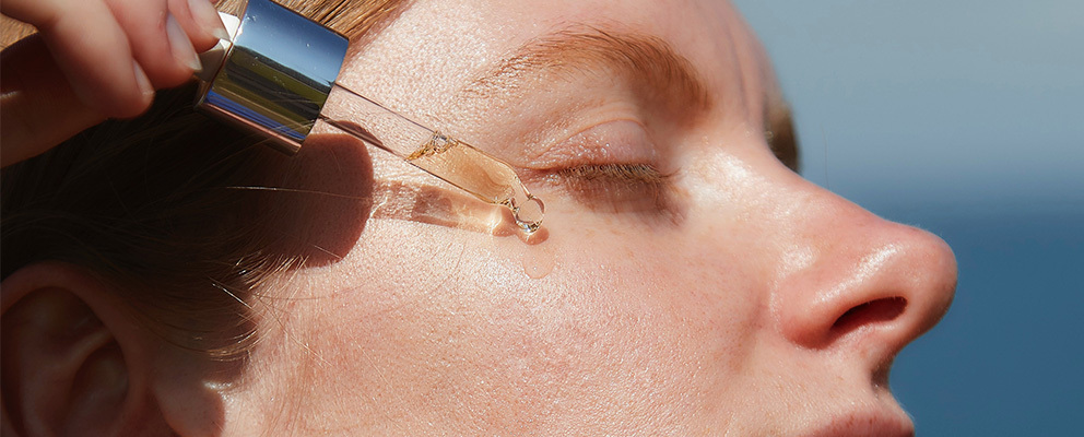 Woman holding oligoperformance serum dropper to her cheek.