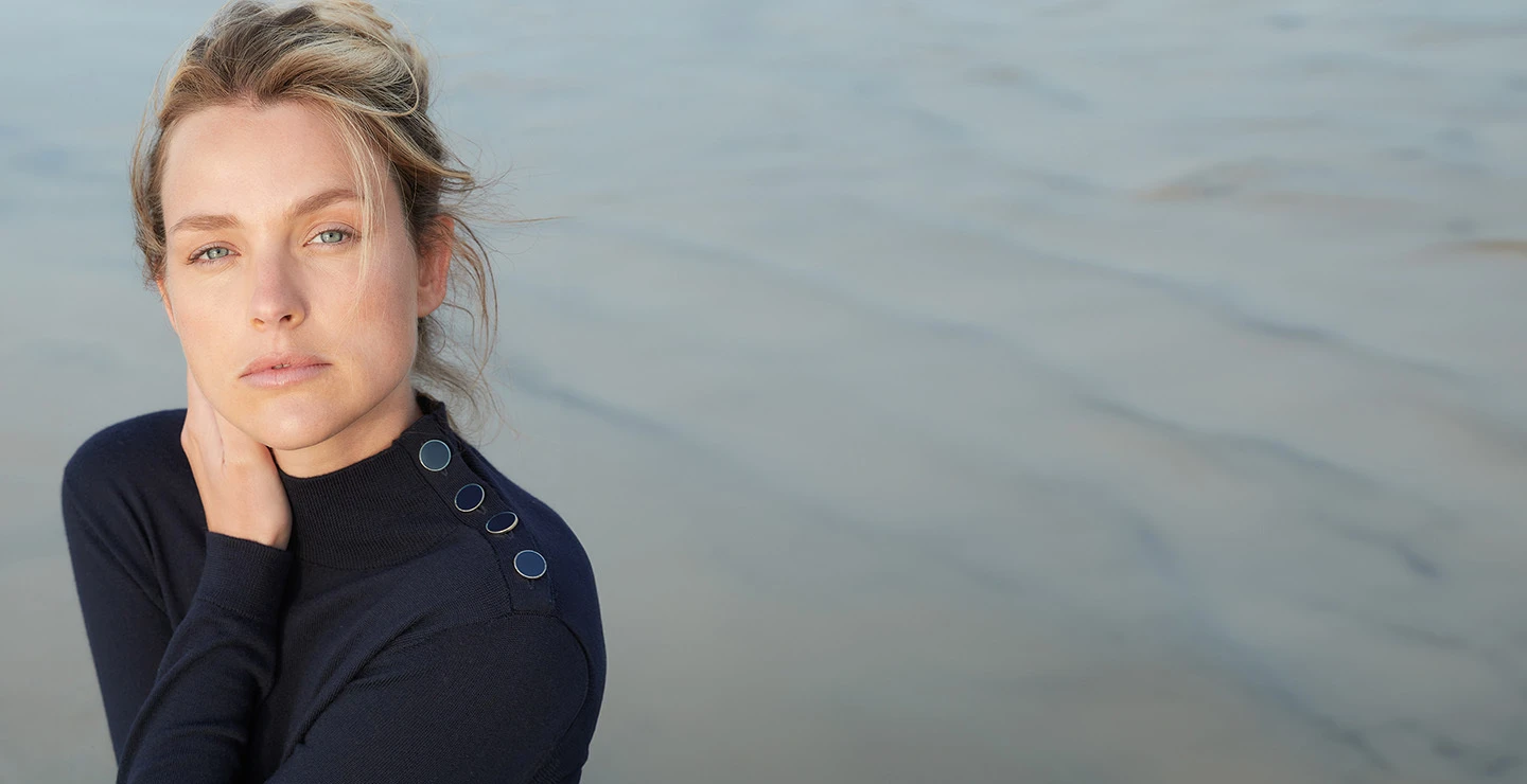 Woman at the beach in sweater, holding her neck and chin.