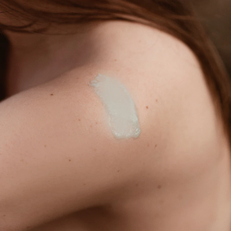 Woman with a dollop of body cream on her bare shoulder.