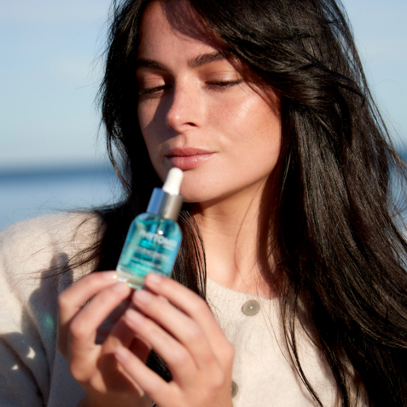 Woman with long wavy hair, gazes down at a Phytomer Hydracontinue 12H Moisturizing Flash Gel. 