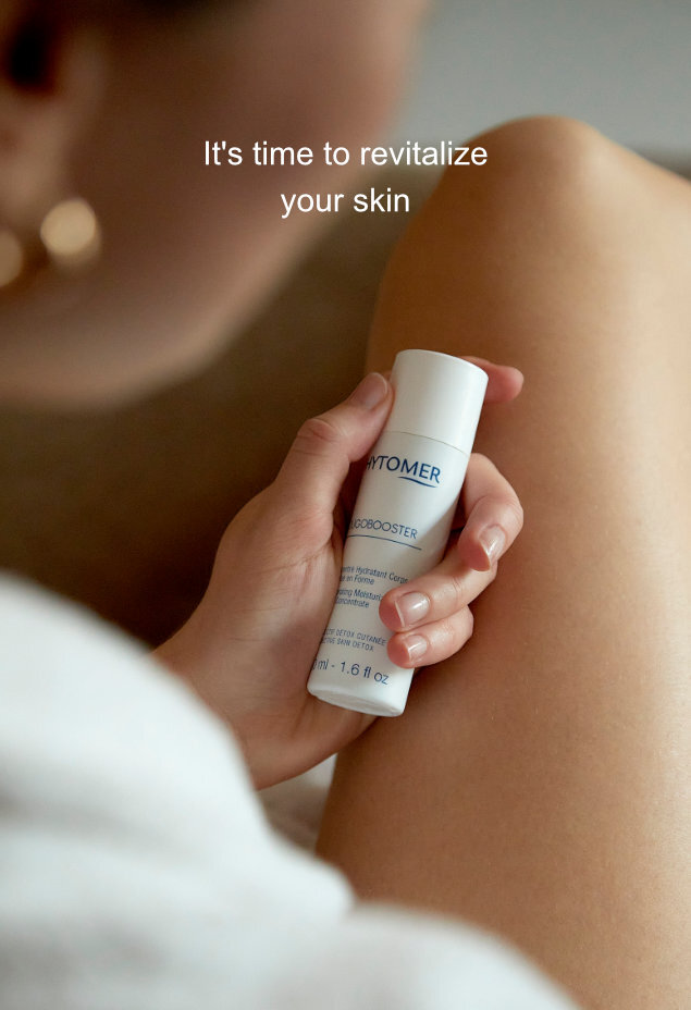 A woman holds a 50 milliliter Oligobooster Invigorating Moisturizing Body Concentrate in her lap. An overlapping title reads It's time to revitalize your skin. 