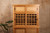 Close-up of grid glass sliding doors and drawer handles on Japanese-style Mizuya tea chest in teak finish.