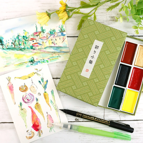2 watercolor paintings, a landscape & an illustration of carrots, next to 6 watercolor pans, a waterbrush, a fineline pen, & a green washi tape box.