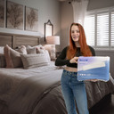 Female model holding bag of Incontrol Booster Pads in front of a bed.