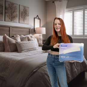 Female model holding bag of Incontrol Booster Pads in front of a bed.