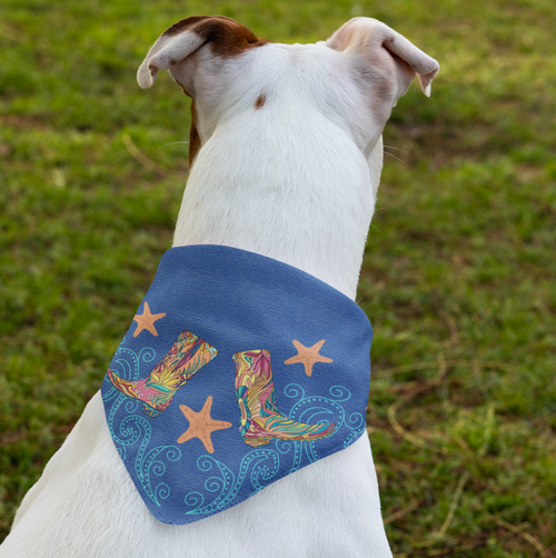 Back of white dog on green grass; dog is wearing blue denim dog bandana with colorful pink cowboy boots and orange sea stars