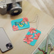 Baggage identification tags on table showing the two sided print: a monogrammed front and colorful floral design on back
