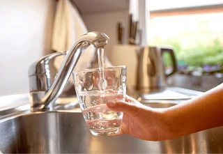 A person filling a glass with clean water from a kitchen faucet