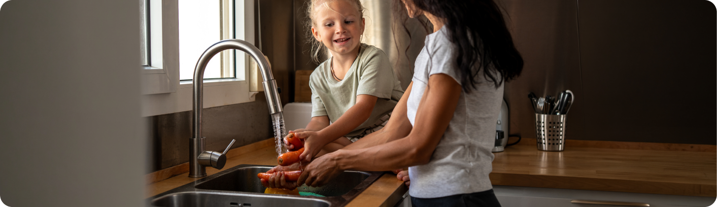 Parent and child washing produce at the kitchen sink