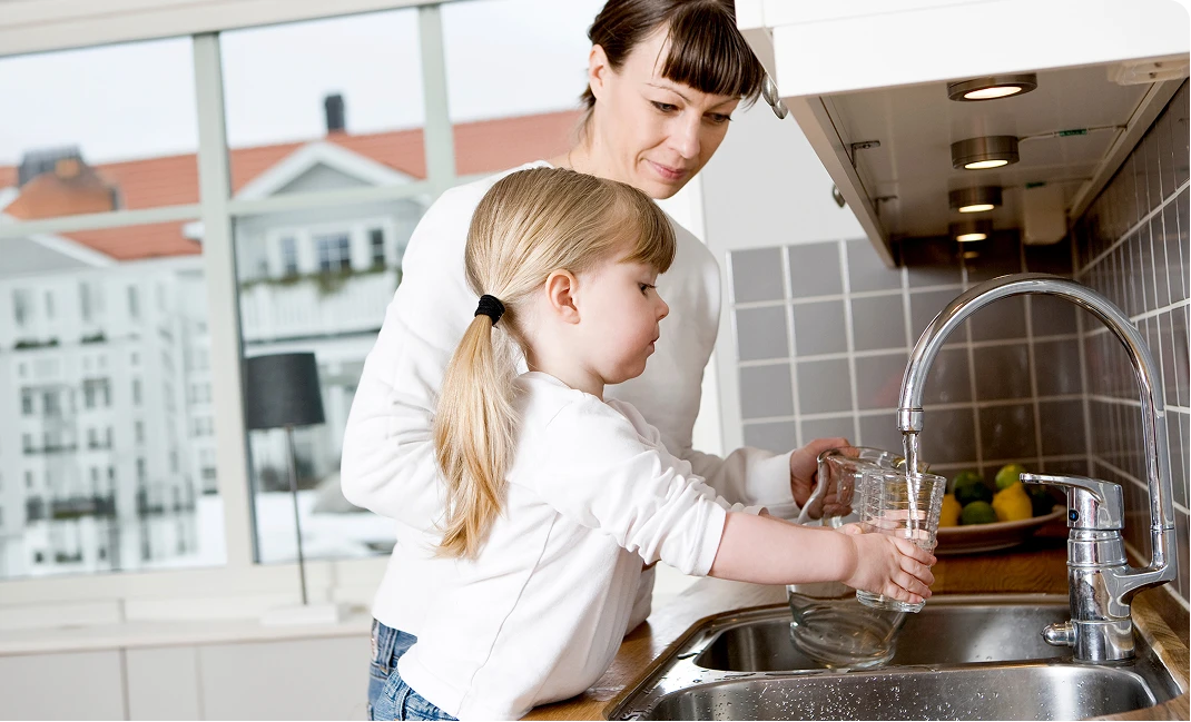 A mother and child washing their hands together at a kitchen sink