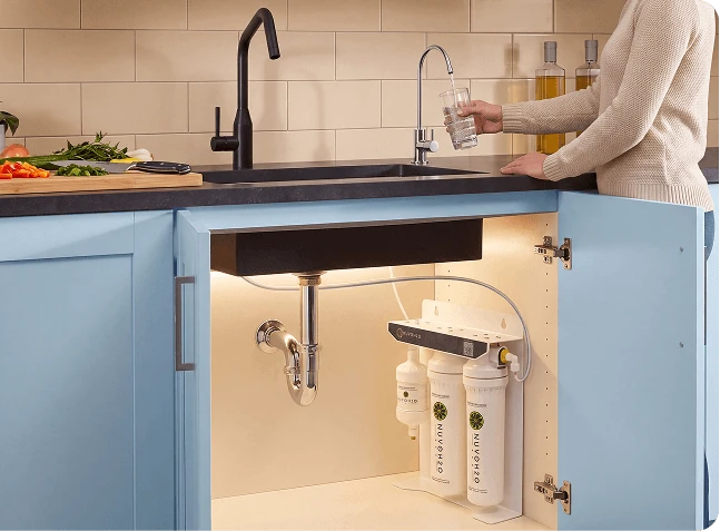 A kitchen sink area showing the NuvoLuxe under-sink filtration system installed