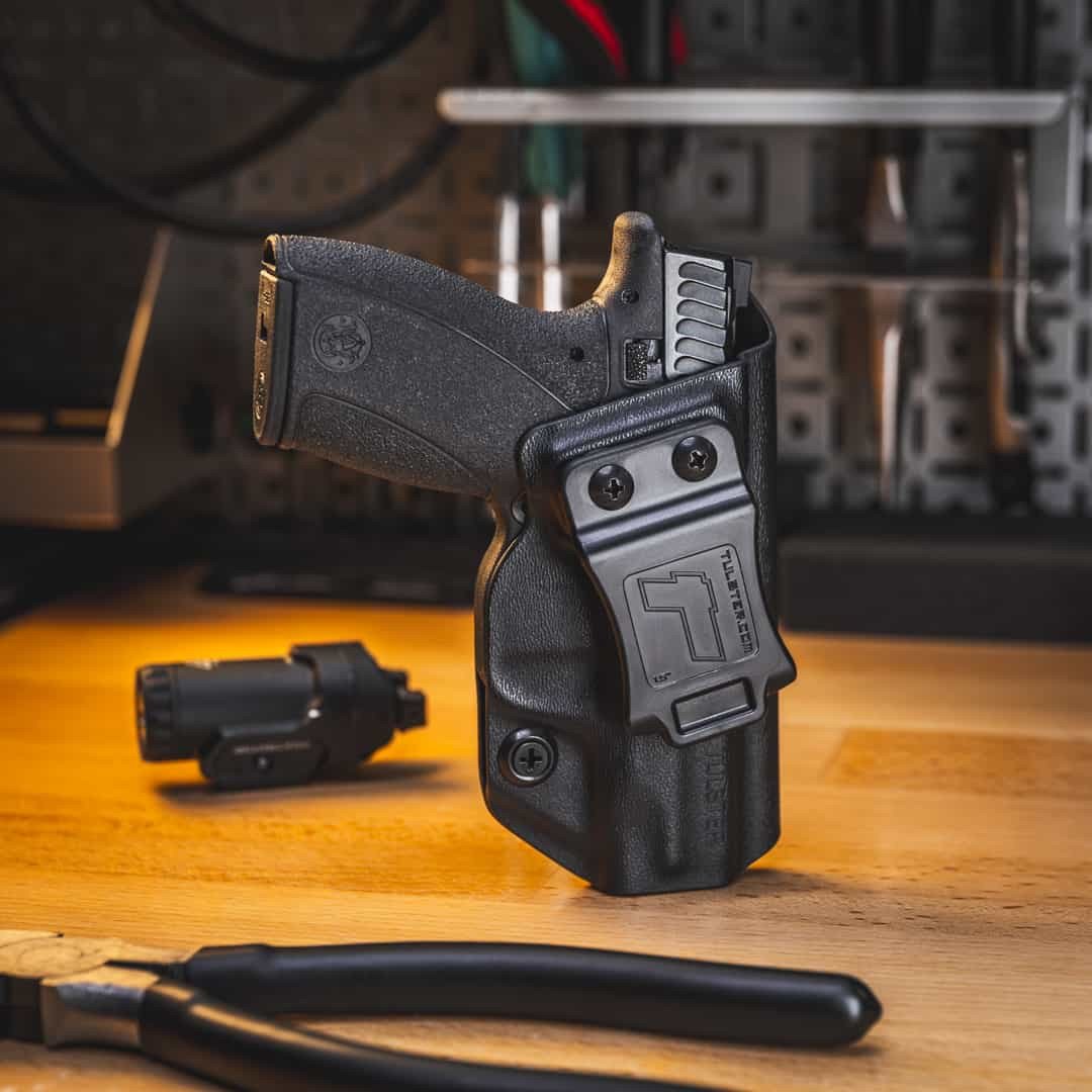 A Smith & Wesson Bodyguard 2.0 in a Tulster Profile inside-the-waistband (IWB) holster sitting on a table next to a Streamlight weapon light.