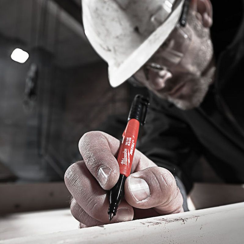 Builder in a hard hat using a Milwaukee Inkzall Jobsite Marker to write on timber.