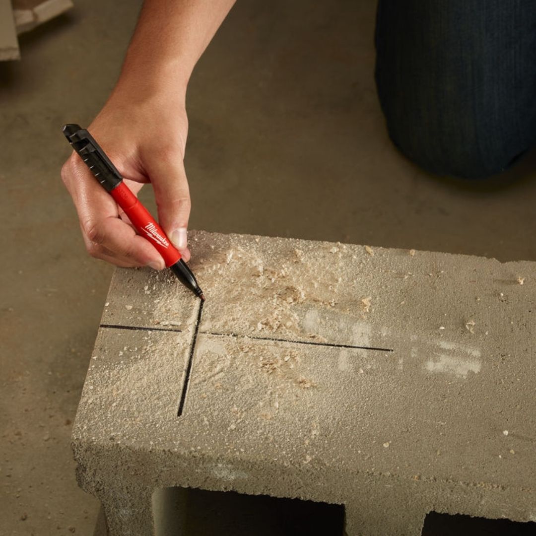 Over head shot of a person using a Milwaukee Inkzall Jobsite Marker to write on dusty sawdust debris covered wood