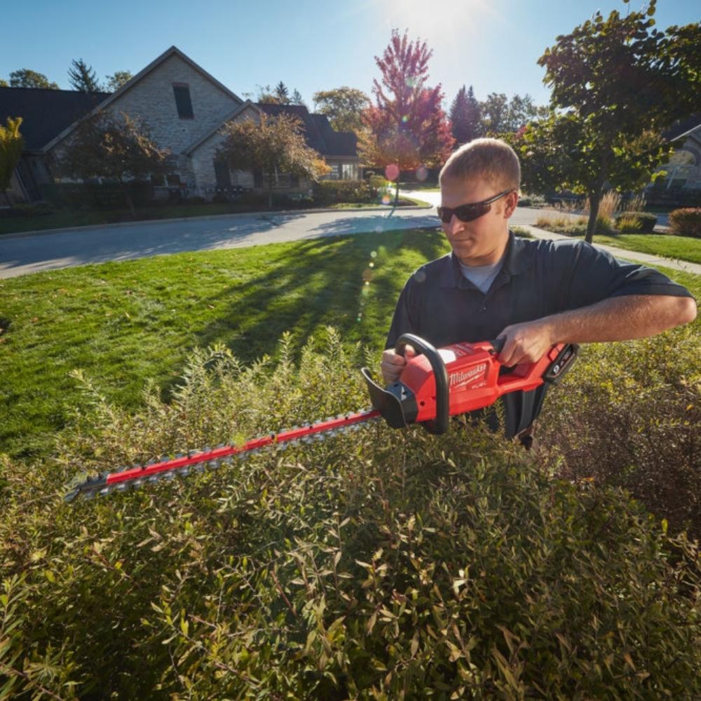 Gardener using milwaukee hedge trimmer to trim the tops of bushes