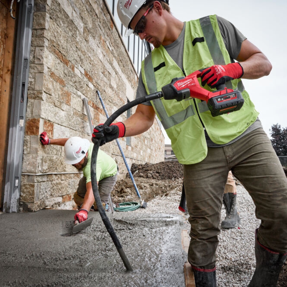 Builder wearing milwaukee hat, hi vis and gloves installing concrete subfloor with the 18v cordless concrete shaker.