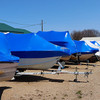 Boats protected with blue marine shrink wrap for winter storage at a marina and boat dealership