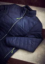 A navy jacket with a quilted design and a green zip pull, laid flat on a textured surface.