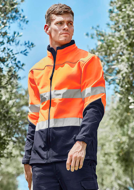 A hi-vis softshell jacket in bright orange and navy, featuring reflective stripes and a zipped front, worn by a model outdoors.