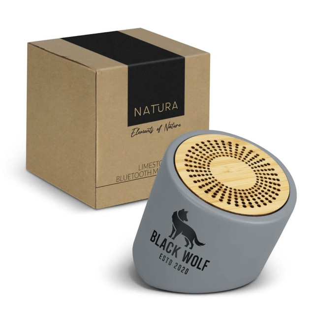 A grey Bluetooth mini speaker with a wooden top, next to a sturdy brown box featuring branding.