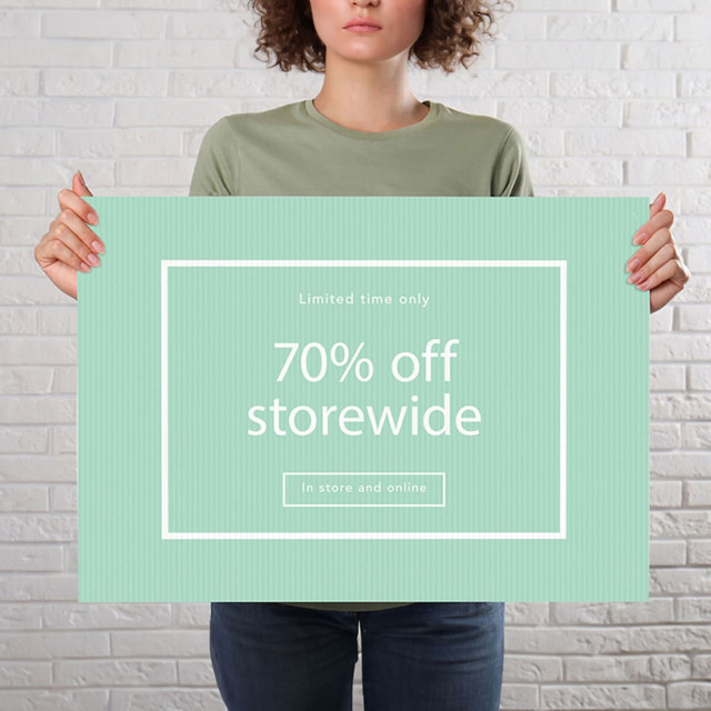 A person holds a large green sign with a white border, featuring a promotional message about storewide discounts.