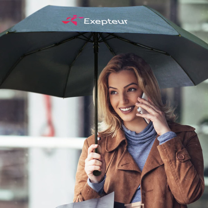 A green umbrella held by a woman talking on a phone, featuring a logo on the canopy.