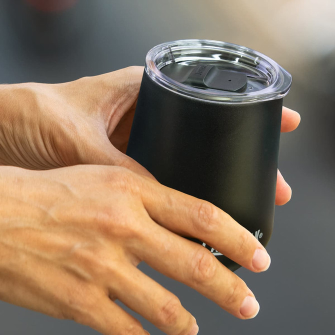 A drink bottle in matte black with a clear lid, held in a person's hand, featuring a logo.