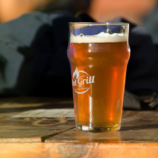 A transparent beer glass filled with amber-coloured beer, featuring a logo and set on a wooden table.