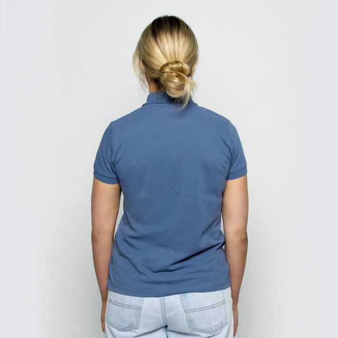 A back view of a women's polo shirt in a soft blue colour, featuring a fitted design and short sleeves.
