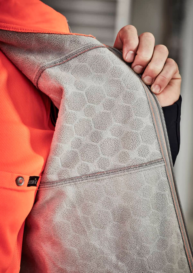 A close-up of an orange unisex softshell jacket showcasing a grey interior with a honeycomb texture and a zipper.