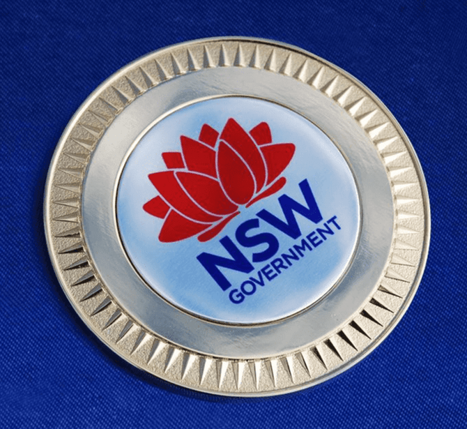 A 70mm medallion featuring a logo, set against a blue velvet background.