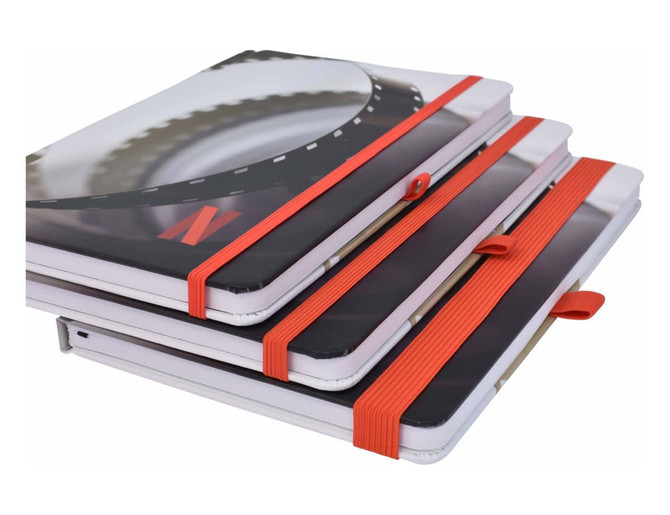 A stack of three A5 notebooks with full colour matte covers, featuring orange elastic closures.