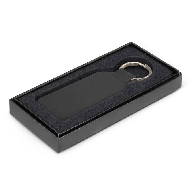 A rectangular black leather key ring displayed in a sleek black box with a soft interior.