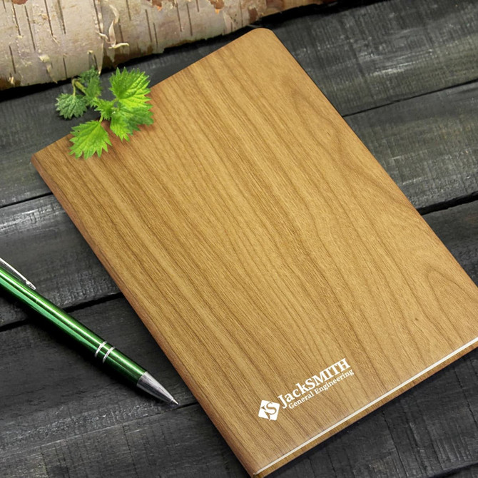 A wooden-textured notebook with a logo on the cover, accompanied by a green pen and a small leafy sprig.