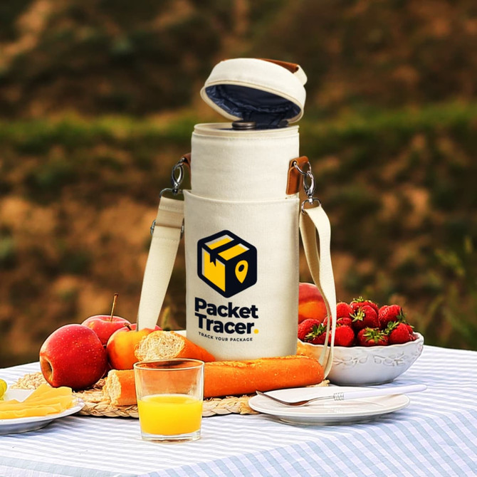 A cream wine cooler bag with a logo, resting on a picnic table surrounded by apples, strawberries, bread, and juice.