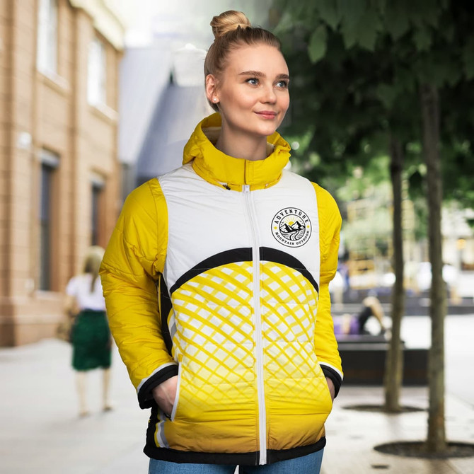 A woman is wearing a custom reversible puffer jacket in yellow and white, featuring a logo and a modern design.