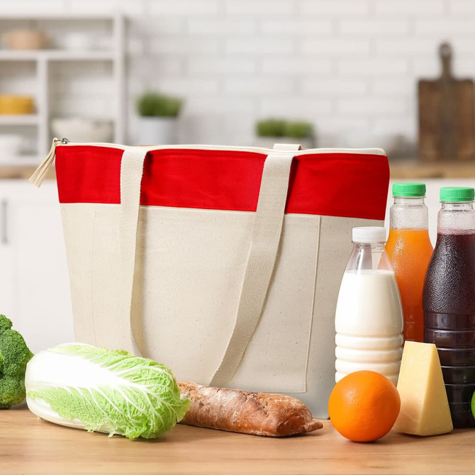A cotton tote in natural and red, surrounded by fresh produce, drinks, and a loaf of bread. It has a logo.