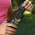 A drink bottle with a black matte finish, featuring a logo, held by a person outdoors.