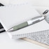 A metal pen with a white barrel and grey grip, placed on a notepad among other stationery items.