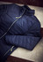 A dark navy quilted jacket laid flat with a zip closure and a high collar on a textured surface.