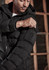A black unisex puffer jacket with a hood, featuring a zip-up front and a pocket on the arm.