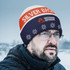A custom knitted beanie in orange and navy blue with a logo, featuring snowflake patterns on the lower part.