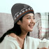 A grey custom knitted beanie with a mountain and bear design, worn by a smiling person holding a drink.