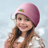 A pink brushed kids beanie sits atop a smiling girl's head, featuring a logo on the front.