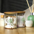 Round glass storage canisters with wooden lids, containing cotton tips and other items, with a logo present.