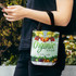 A small tote bag with a vibrant design featuring fruits and vegetables, predominantly in green and white, with a black handle.
