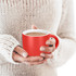 A red coffee mug held in hands, featuring a contrasting white interior. The background shows a knitted sweater.